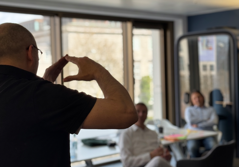 Person gestikuliert während einer Präsentation oder eines Workshops vor mehreren sitzenden Teilnehmenden in einem Workshop.