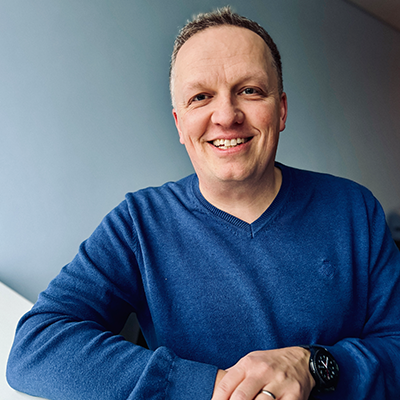 Wir sehen Holger Richter, Associate Partner und Senior Head of Microsoft Analytic, der entspannt in die Kamera lächelt