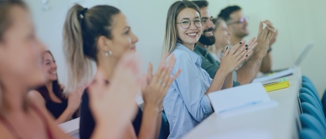 Teilnehmende einer Schulung applaudieren in einem modernen Seminarraum.