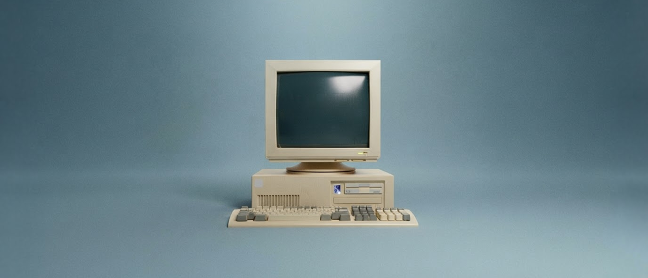 Retro-Desktopcomputer mit Röhrenmonitor, Rechner und Tastatur vor hellblauem Hintergrund. Der beige Computer im Stil der 1980er- und 1990er-Jahre steht frontal im Bild, der Bildschirm ist ausgeschaltet.